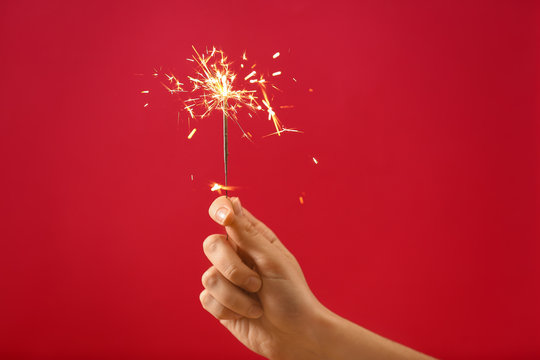 Female Hand With Christmas Sparkler On Color Background