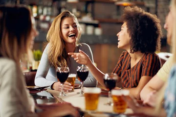 Gordijnen Multicultural friends sitting in restaurant and drinking wine and beer. © chika_milan