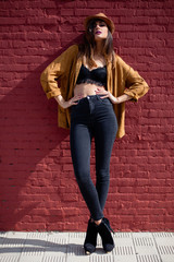 Beautiful young woman with hat standing in front of red wall.