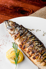 grilled mackerel with a slice of lemon on a white plate in a beautiful composition on a brown table covered with sacking. close-up. Georgian cuisine