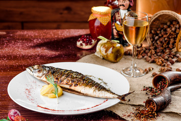 grilled mackerel with a slice of lemon on a white plate in a beautiful composition on a brown table covered with sacking. close-up. Georgian cuisine