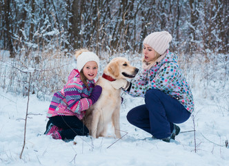 Fototapeta na wymiar Cheerful mom and her cute daughter with their dog golden retriever in winter