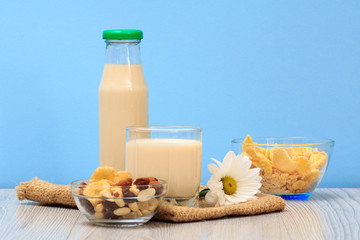 Bottle and glass of milk, bowls with muesli and cornflakes on sackcloth.