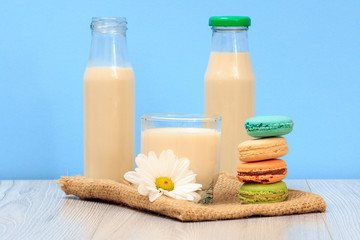 Obraz na płótnie Canvas Bottles and glass of milk with macaroons on sackcloth in blue background.