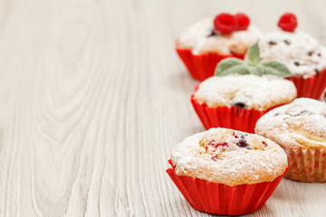 Homemade fruit muffins sprinkled with powdered sugar on wooden desk.