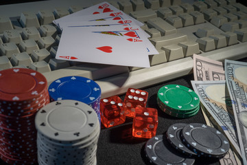 Playing cards, dice, US dollar banknotes, poker chips surrounding computer keyboard, online gambling 