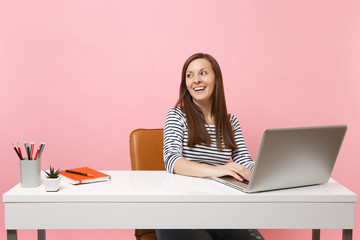 Young joyful happy woman looking aside working on project while sitting at office with pc laptop...