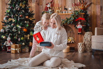 Merry Christmas Happy Holidays Cheerful mom her cute daughter girl exchanging gifts. Parent little child having fun near Christmas tree indoors. Morning Xmas. Portrait family close up.