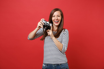 Obraz premium Portrait of joyful beautiful young woman in striped clothes holding retro vintage photo camera isolated on bright red wall background. People sincere emotions, lifestyle concept. Mock up copy space.