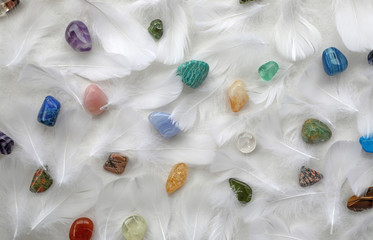 Obraz na płótnie Canvas High Resonance Healing Crystals Cleanse - randomly scattered tumbled multi coloured healing stones and fluffy white feathers creating a holistic background 