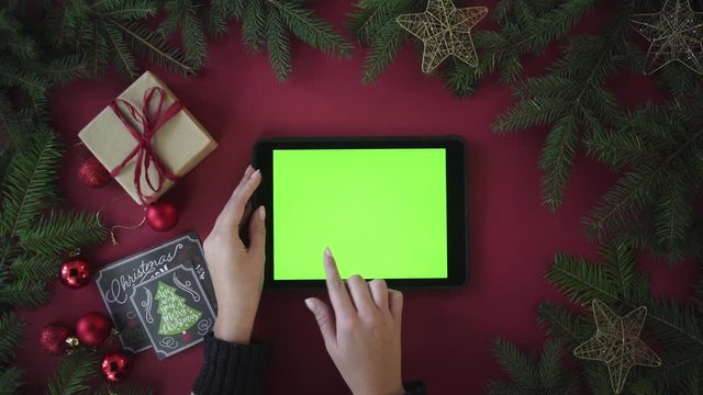 Christmas table top view from above. Tablet with green screen. Woman slide images and zooming. Different gestures. Red background with garland. Chroma key