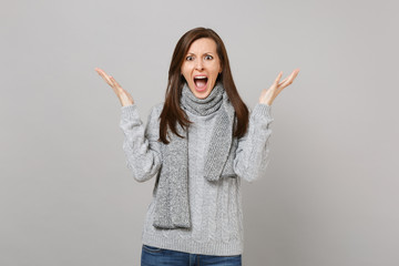 Shocked young woman in gray sweater scarf screaming, spreading hands isolated on grey background in studio. Healthy fashion lifestyle, people sincere emotions, cold season concept. Mock up copy space.