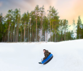 winter, leisure and entertainment concept - happy young man sliding down hill on snow tube over natural background