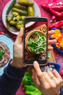 Phone food photography. Woman hands take a photo of lunch or dinner with smartphone for social networks or blogging in trendy top view style. Mobile phone screen. Vegan vegetarian healthy food