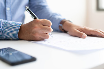 Closeup of male candidate filling in application form. Business person sitting at desk. Recruitment concept. Cropped view.