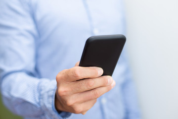 Closeup of man holding and using smartphone. Person texting on digital gadget. Technology and communication concept. Cropped front view.