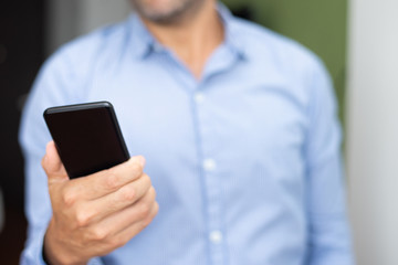 Closeup of man networking on smartphone. Person holding digital gadget. Technology and communication concept. Cropped front view.