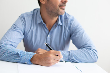 Closeup of pensive business man writing on sheet of paper. Paper sheet lying on desk. Application concept. Cropped front view.