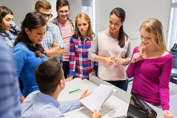 education, high school, technology and people concept - group of students and teacher with papers and laptop computer in classroom