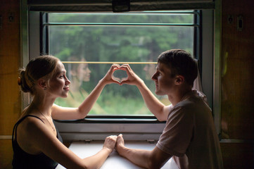 Couple of lovers traveling in train. Mood portrait of romantic pair in wagon looking at window with self reflections in it. Adventure on holiday of happy friends. Man and woman looking at each other.