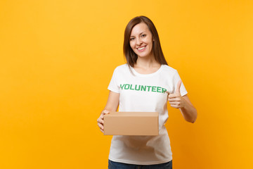 Fototapeta na wymiar Portrait of smiling woman in white t-shirt with written inscription green title volunteer with blank cardboard box isolated on yellow background. Voluntary free assistance help, charity grace concept.