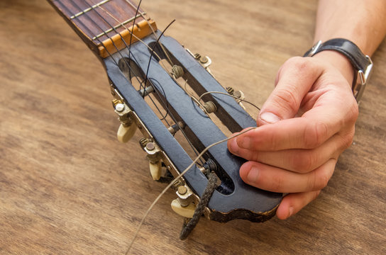 Lute maker shop and classical music instruments: young adult artisan fixing old classic guitar adding a cord and tuning the instrument. Close up of hands and palette