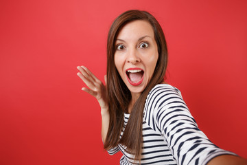 Close up selfie shot of excited young woman spreading hands, keeping mouth wide open, looking surprised isolated on red wall background. People sincere emotions, lifestyle concept. Mock up copy space.