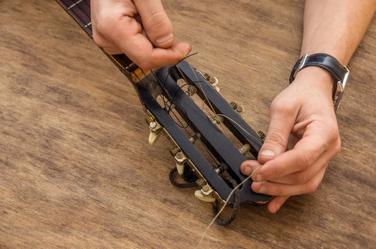 Lute maker shop and classical music instruments: young adult artisan fixing old classic guitar adding a cord and tuning the instrument. Close up of hands and palette
