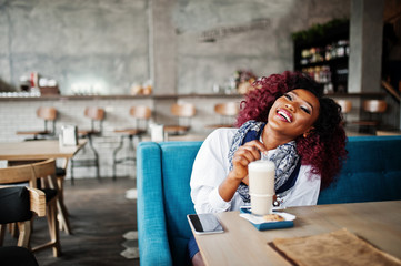 Fototapeta na wymiar Attractive african american curly girl sitting at cafe with latte.