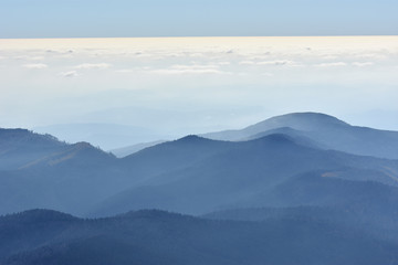 Peaceful blue nature background with foggy Bucegi mountains in Carpathians seen from Cota 2000, Sinaia resort, Romania
