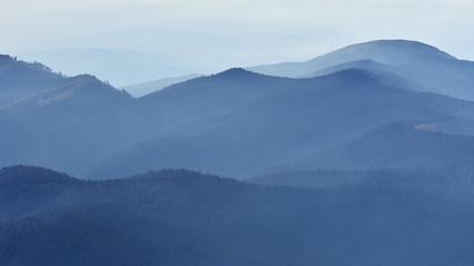 Peaceful blue nature background with foggy Bucegi mountains in Carpathians seen from Cota 2000, Sinaia resort, Romania