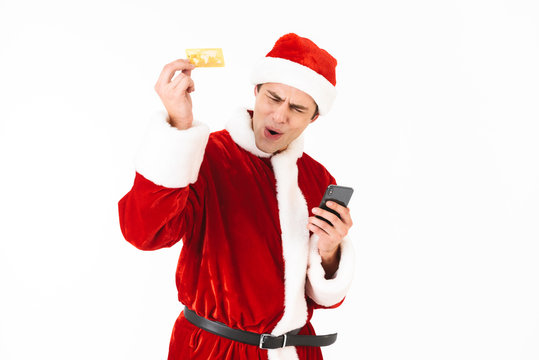 Image of joyous man 30s in santa claus costume holding smartphone and credit card, isolated on white background in studio
