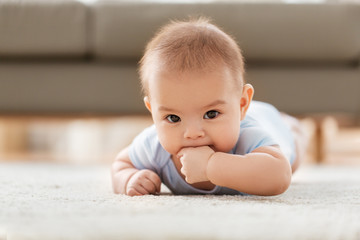 babyhood, childhood and teething concept - sweet little asian baby boy lying on floor at home
