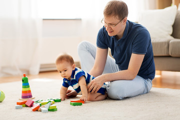 family, fatherhood and people concept - happy father with little baby son playing with toy blocks at home
