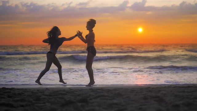 Two girls exercise, training karate on ocean beach against sunset sky and rolling waves