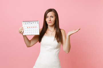 Puzzled guilty bride woman in wedding dress spread hand hold female periods calendar for checking menstruation days isolated on pink background. Medical, healthcare, gynecological concept. Copy space.