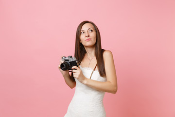 Dreamy bride woman in wedding dress looking up holding retro vintage photo camera choosing staff, photographer isolated on pink background. Wedding to do list. Organization of celebration. Copy space.