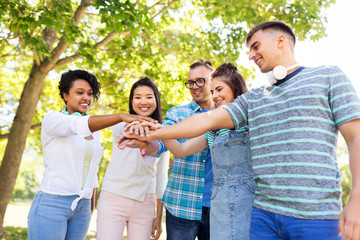 people, friendship and international concept - group of happy smiling friends stacking hands in park