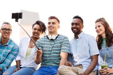 technology, friendship and international concept - group of students or friends with drinks taking picture by smartphone on selfie stick in city