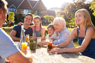 Multi Generation Family Sitting At Table Enjoying Outdoor Summer Drink At Pub