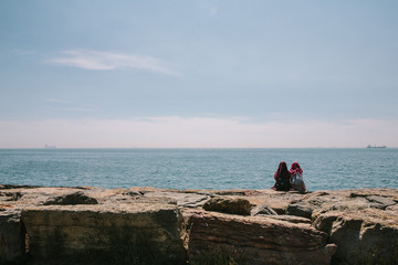 Two young Turkish girls in hijabs are sitting on the embankment of the Asian side of Istanbul, talking and admiring the sea. Istanbul, Turkey