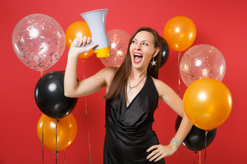 Funny young woman in little black dress celebrating, looking up, holding megaphone on red...
