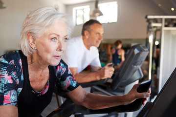 Fototapeta na wymiar Active Senior Couple Exercising On Cycling Machines In Gym