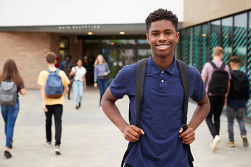 Portrait Of Smiling Male High School Student Outside College Building With Other Teenage Students...