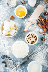 Christmas and winter baking background. Kitchen utensils and ingredients for cooking baking - flour, sugar, eggs, butter, milk, cinnamon sticks, whisk, rolling pin, anise, Blue concrete background 