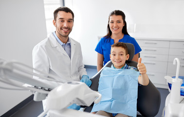 Obraz premium medicine, dentistry and healthcare concept - happy dentist, assistant and kid patient showing thumbs up at dental clinic