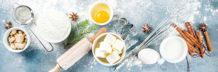 Christmas and winter baking background. Kitchen utensils and ingredients for cooking baking - flour, sugar, eggs, butter, milk, cinnamon sticks, whisk, rolling pin, anise, Blue background banner