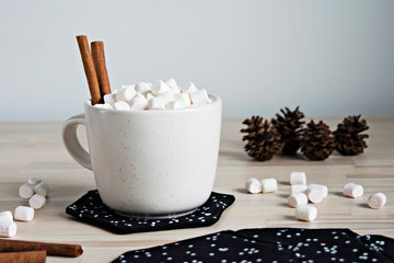 White cup with cinnamon and marshmallows, pine cones and fabric coasters on the table