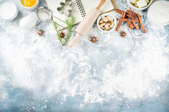 Christmas and winter baking background. Kitchen utensils and ingredients for cooking baking - flour, sugar, eggs, butter, milk, cinnamon sticks, whisk, rolling pin, anise, Blue concrete background 
