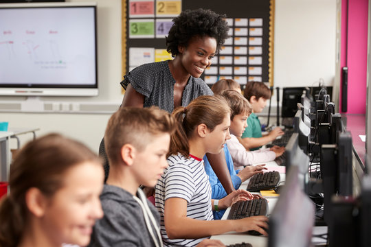 Teacher Helping Female Pupil Line Of High School Students Working at Screens In Computer Class